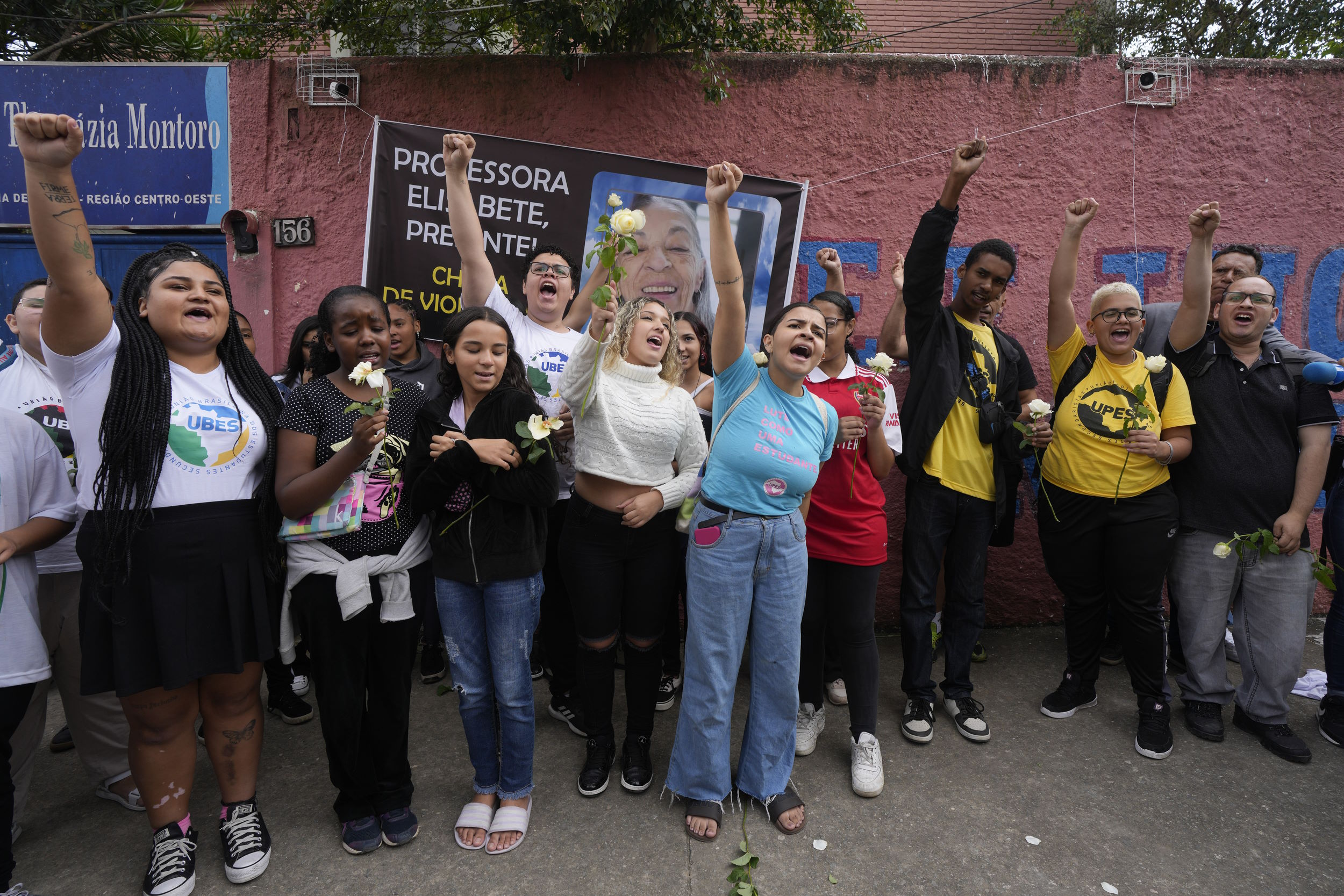 Brazil school violence: Middle school age children stand with fists raised and protest signs om front of red brick wall