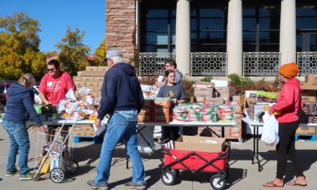 Child poverty: Several people stand around outside in front of a brick building surrounding large tables stacked with packaged food - one man pulling a red wagon .