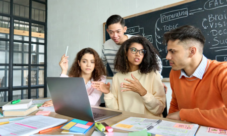 iCivics curridylum: Four older students sit around laptop at table covered in multi-colored note papers in active discussion