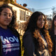 Ethnic sipport middle school girls: A young woman and two young teen girls stand next to each other outside in front of a multistory building on a sunny day