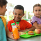 Summer EBT in schools, school meals: Three elementary children sit at table with lime green trays earing lunch