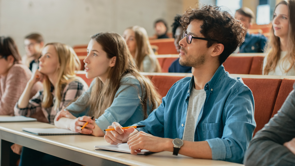 Autistic students college success tips: Several college students sit at rows of desks on risers