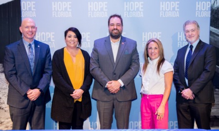 Mentoring month: 3 men and 2 women in business cloths stand in front of floor to ceiling light blue screen with white Hope Florida logo repeat printed across several rows