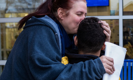 Student psychiatric evaluations: Woman with long red hair in ponytail and navy sweatshirt hugs and kisses forehead of young boy with black hair