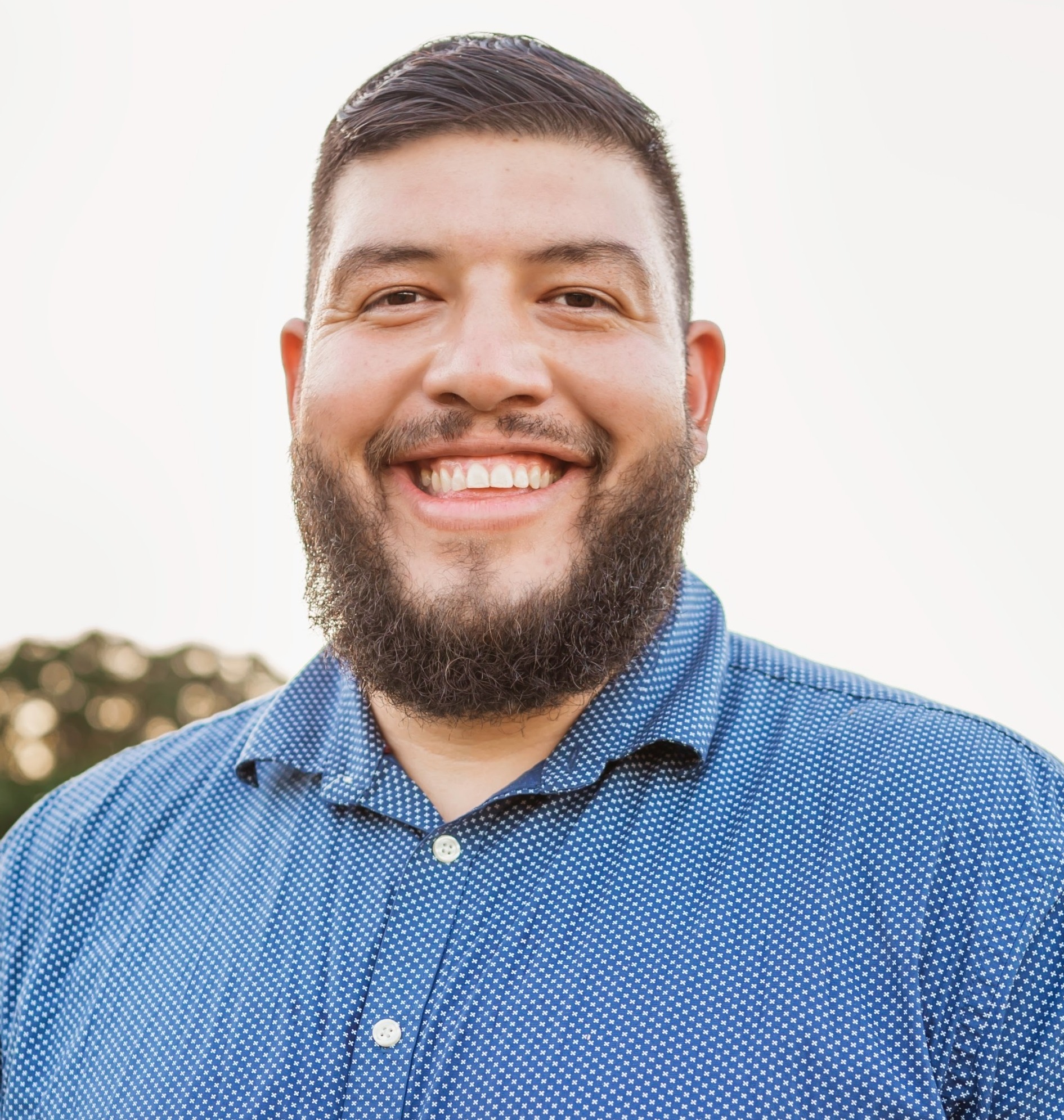 AI afterschool: Headshir of man with brown hair and beard in blue polo shirt smiling widely into camera