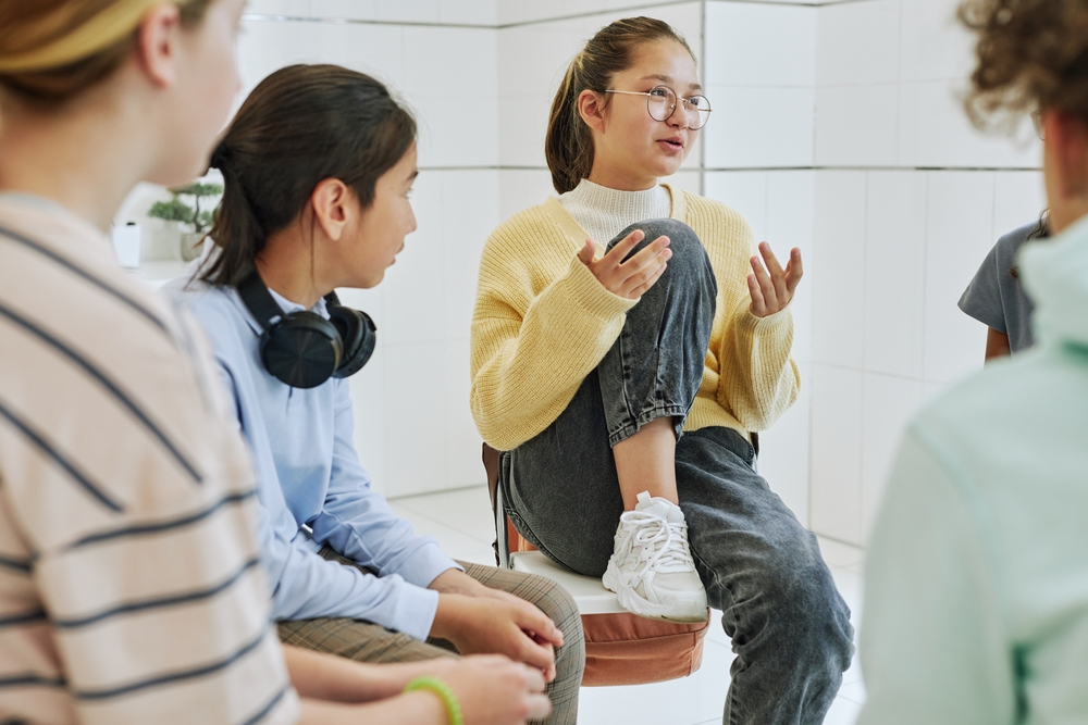 Student-led mental health: Portrait of teenage girl sharing feelings in support group circle of 4 other teens