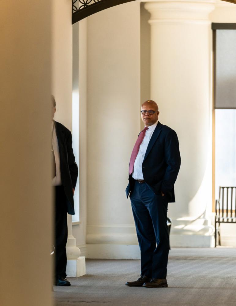 Juvenile Justice lawyers Ohio: Attorney Bill Beck, black man in black suit, white shirt and red tie, stands with hands in pockets, between large pillars in large hallway of cream building