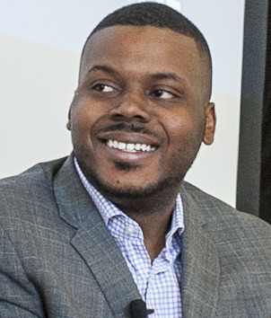 Guaranteed Income: Headshot Black man with short black hair, short black beard and mustache, in medium gray suit and light blue shirt