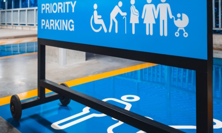 Universal Design: Bright blue metal sign on wheels in indoor parking lot, with white text "Priority Parking" and 6 white disability icons