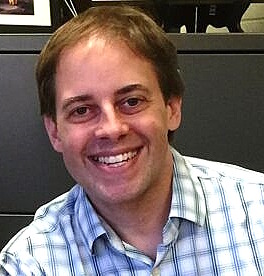 Teen survey depression: Headshot of smiling man with brown hair in blue and white plaid shirt