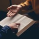 Chaplains in school: Closeup of hands of two people seated across from each other with one persons folding and reading Bible and the other gesturing with their hand towards the Bible