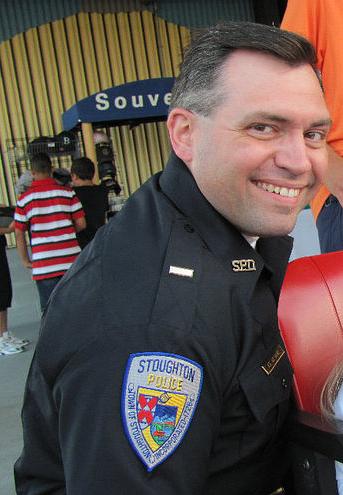 Sandra Birchwood justice: headshot of smiling man with graying dark hair in black police uniform with police department patch on upper right sleeve