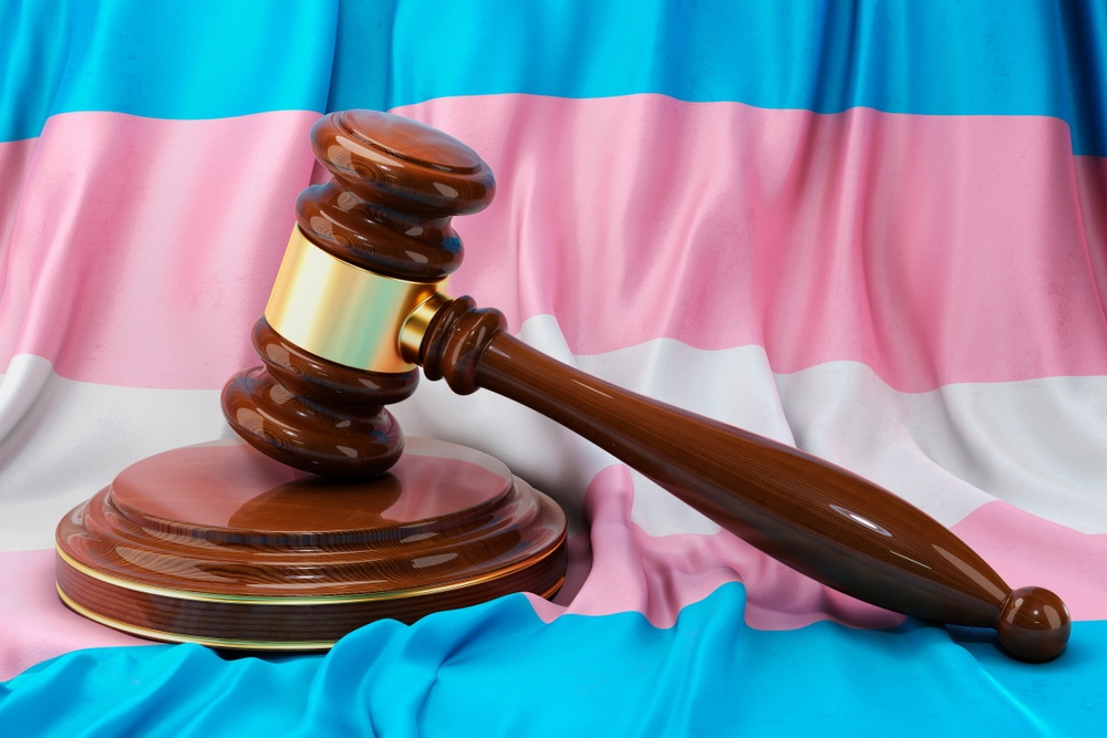 Transgender locker room ruling: Transgender flag with white, pale blue and pale pink stripes sits behind a brown wood courtroom judge's gavel