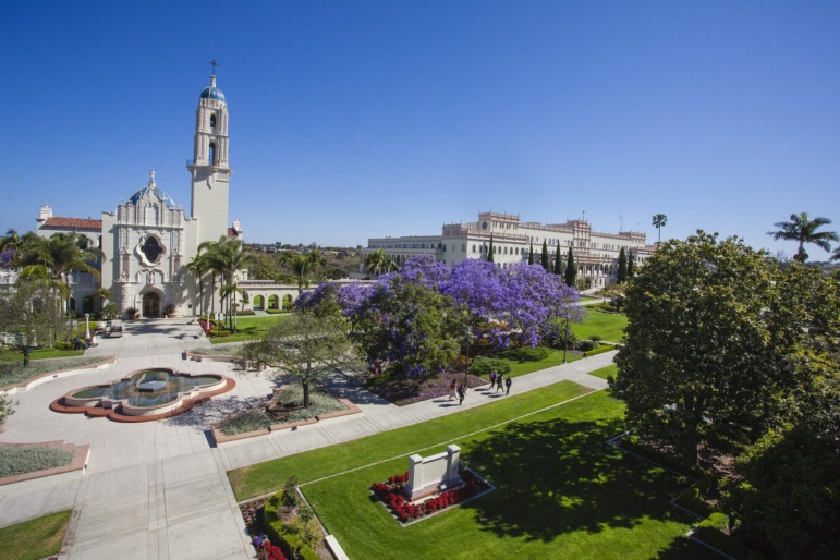 Neurodivergent student empowerment in college: Long view of a college campus with traditional buildings and quadrangle area surrounded by lawns and green trees under a clear blue sky