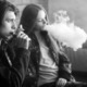 Colorado Vaping Lawsuit settlement: Black and white photo of two older teens sitting against brick wall smoking electronic cigarettes