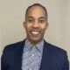 Ivan Heredia newsmaker headshot; smiling man in suit jacket and patterned, collared shirt