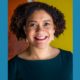 Elizabeth Lindsey newsmaker headshot; african american woman with curly hair and earings in dark blue shirt on orange background