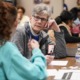 Nonprofits scramble for help amid dearth of volunteers: older person with gray hair and glasses rests head on hand while talking to someone