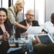 Post-Pandemic Nonprofit: Group of 6 people in active discussion sit & stand around conference table