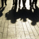 No Place for Kids; Silhouette of feet and legs abd their full body shadows of four people in cobblestone walkway