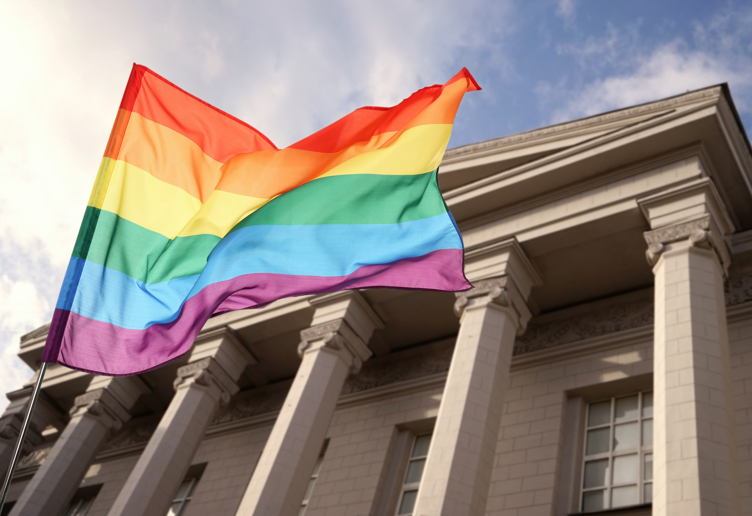 LGBTQ+ youth, students and Title IX: Rainbow flag closeup with traditional style, pillared building in the background