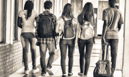 school segregation levels: Back view of teens with school backpacks walking away from camera in a school hallway