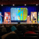 Arts in STEM: Several teens in costumes stand on theater stage with five pieces of art all larger than a person