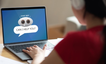 AI & student creativity research: Over shoulder shot of unrecognizable student with wireless headset sitting at desk at home, using chat bot on computer laptop, typing on keyboard