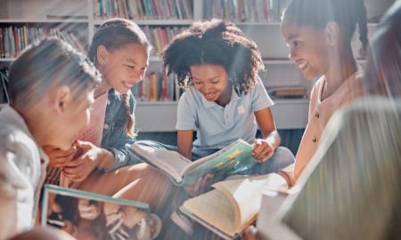 Touch and literacy: Group of middle school students sitting on a library rug in circle reading with sun rays shining down on them