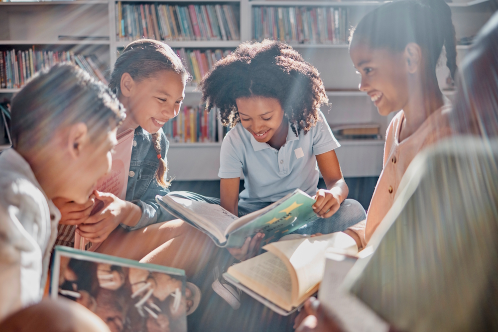 Touch and literacy: Group of middle school students sitting on a library rug in circle reading with sun rays shining down on them