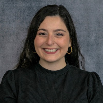 Lie detector tests and juveniles: Headshot young, smiling, woman with long dark hair in black shirt against gray background