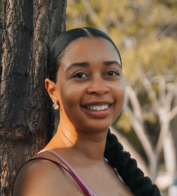 School segregation: Black woman with dark hair pulled back into long braid in sleeveless top leaning against a tree trunk.