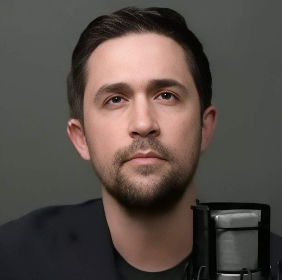 Academic Freedom: Man with dark brown hair, full beard and mustache in collarless black shirt with solemn expression