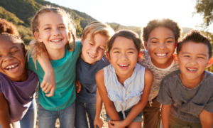 Summer learning strategies: Group of multi-racial preteens standing close to each other outside wearing summer clothes and smiling into camera