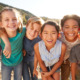 Summer learning strategies: Group of multi-racial preteens standing close to each other outside wearing summer clothes and smiling into camera