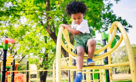 outdoor community spaces grants: young black boy climbs down yellow playground fixture