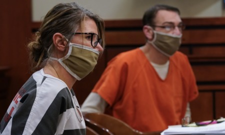 Parents of teen charged in school shooting to stand trial: middle-aged white man and woman in facemasks sit at hearing