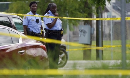 Public heath strategists tackle New Orleans gun violence: two Black cops looking at crime scene beyond yellow tape