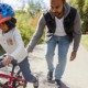 Parenting in America today report: dad helping daughter on bike learn to ride while other daughter films on phone off to the side and mom watches on