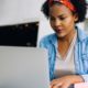 Focused young African female working online with a laptop while sitting at a table in the lobby of a modern office building