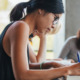 Close up shot of young woman writing notes with classmates studying in background.