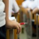 Schools face pressure to take harder line on discipline: closeup of students hand holding red pen with class in desks in background