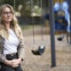 Schools struggle to staff up for youth mental health crisis: female teacher with long hair and glasses sitting on swingset swing