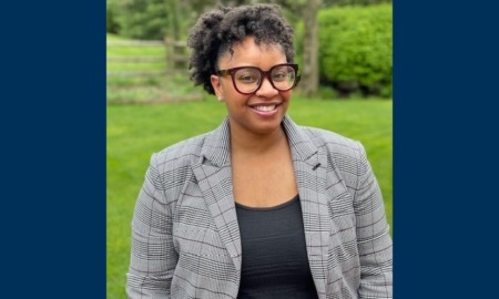 Shereen White: black woman in grey blazer and black glasses standing outdoors smiling