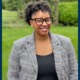 Shereen White: black woman in grey blazer and black glasses standing outdoors smiling