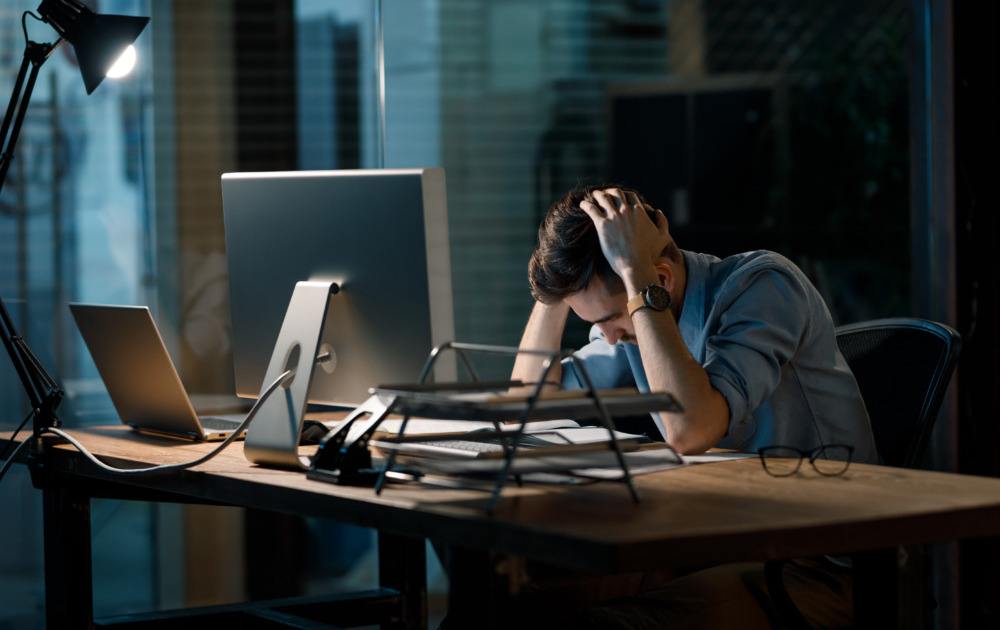 nonprofits misclassify workers: frustrated man with hands on head at computer in dark room