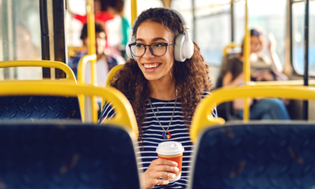 Girl sitting ina a bus drinking coffee, listening to music and looking trough window.