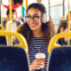 Girl sitting ina a bus drinking coffee, listening to music and looking trough window.