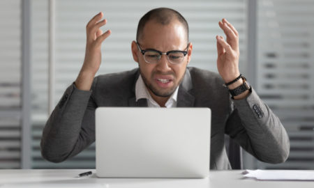 Grant makers hate 4 things: Black man with dark-rimmed glasses wearing gray suit and white shirt sits at silver laptop throwing hands in air with frustrated look