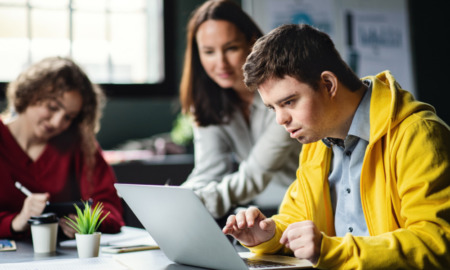 Disabled youth SSI: Young man in yellow jacket, who has Down syndrome, is poised in front of a laptop computer